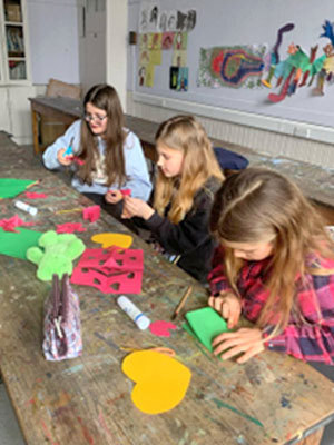 Three girls cutting coloured paper at table